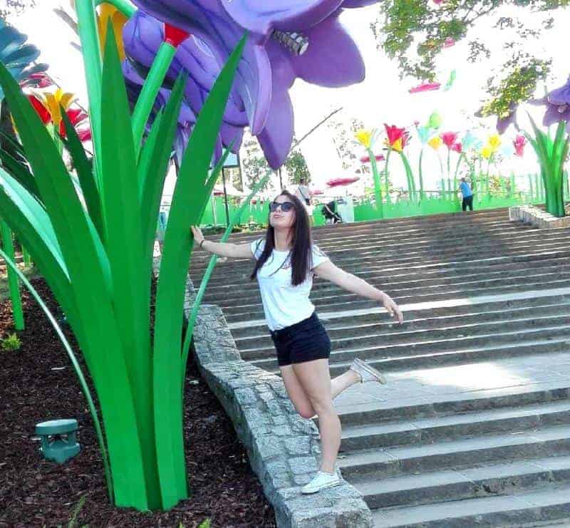 Legendia flower 4 Kobieta pozująca przy gigantycznych modelach kwiatów w parku.