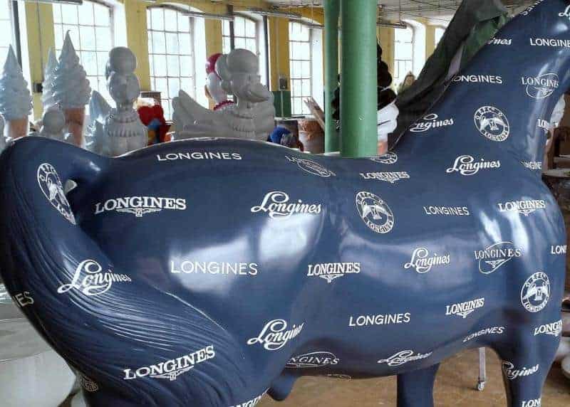 Niebieska rzeźba konia pokryta logo marki Longines w hali produkcyjnej.