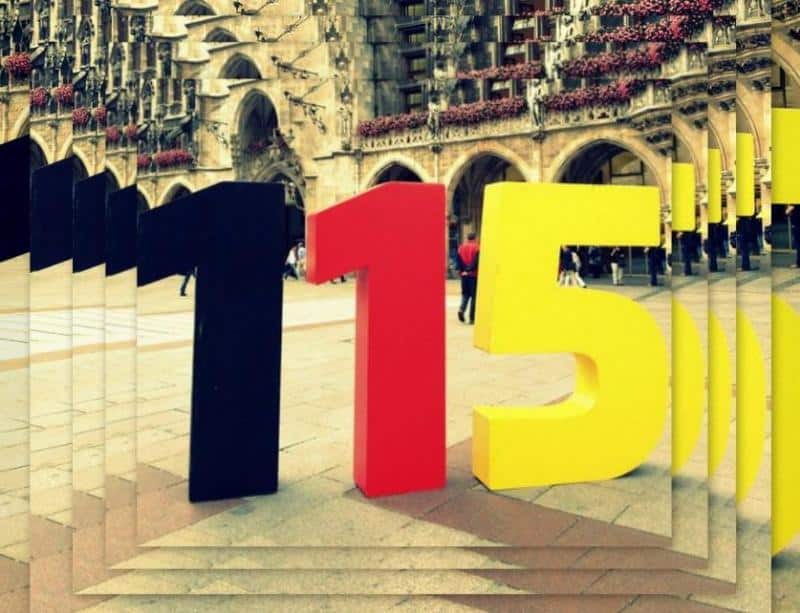 Rzeźby liczb 1, 1, 5 na placu przed zabytkowym budynkiem z łukami i kwiatami.