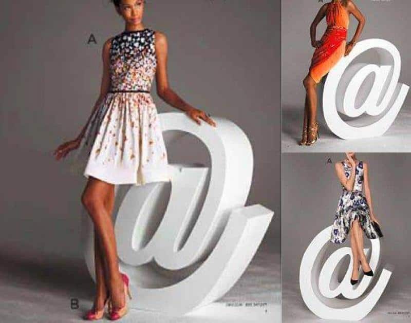 oryg_064490685_1129949550544944_1465385417682452480_o Modelki pozujące w różnych sukienkach obok dużego symbolu '@'.