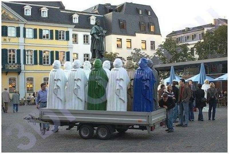 Replika pomnika Beethoven 2 Grupa kolorowych rzeźb na przyczepie na placu miejskim, budynki w tle.