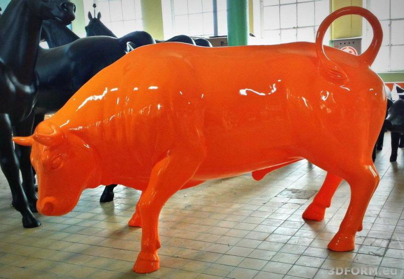 Duża eventowa figura byka 1 Pomarańczowa rzeźba byka znajdująca się w środku, na tle czarnych rzeźb koni