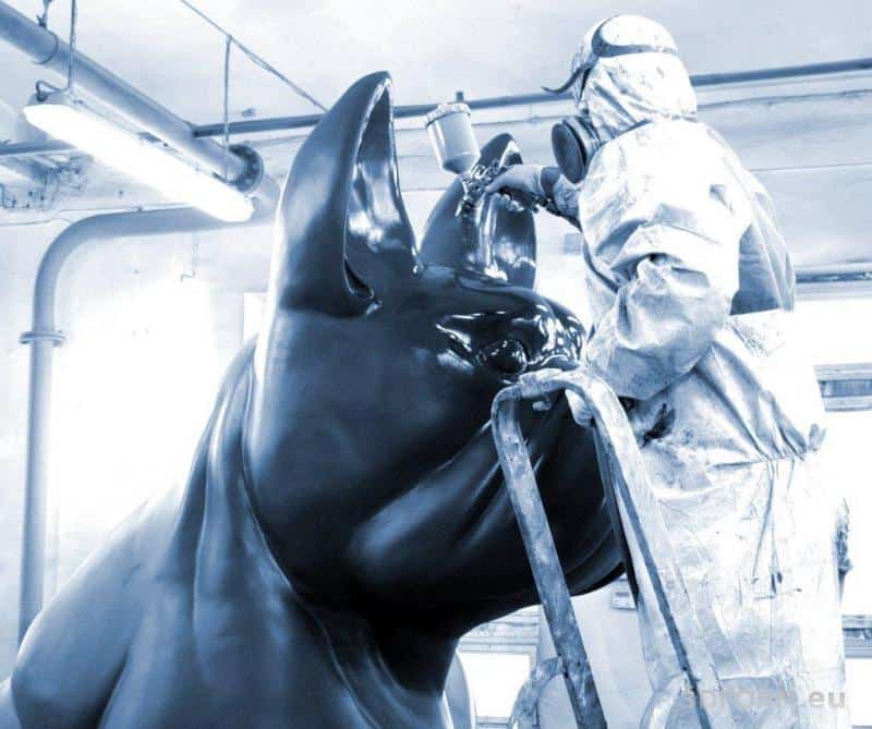 Osoba w kombinezonie maluje dużą rzeźbę psa.