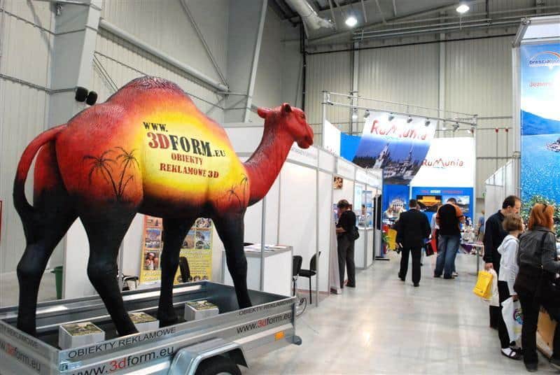 Mobilna makieta wielbłąda 4 Stoisko wystawowe z dużą figurą wielbłąda promującą obiekty reklamowe 3D; w tle kilka stoisk z banerami i ludzie oglądający ekspozycje.