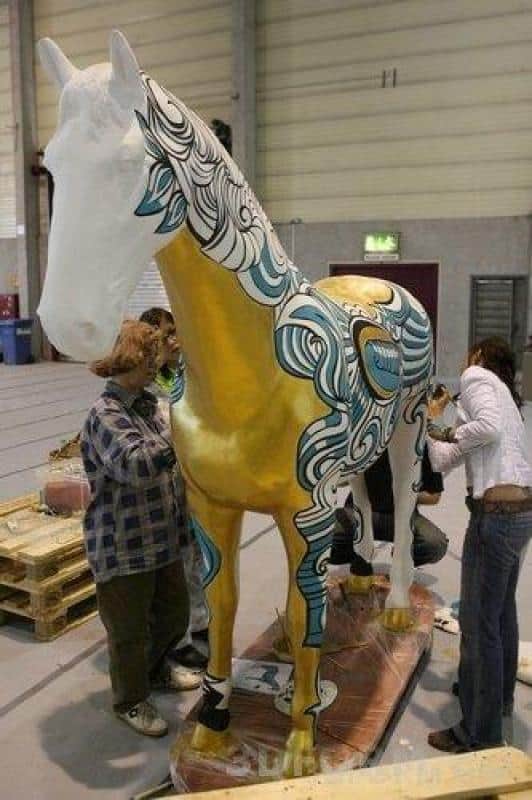 Duże figury malowane przez dzieci 3 Ludzie malujący dużą rzeźbę konia w budynku.