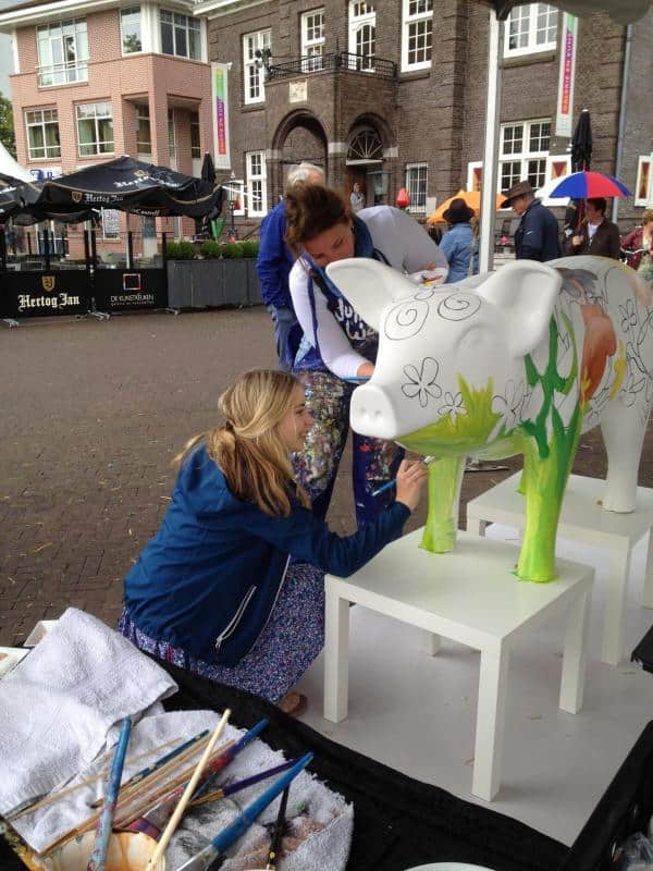 Duże figury malowane przez dzieci 1 Kobiety malują wielką rzeźbę krowy na zewnątrz budynku.