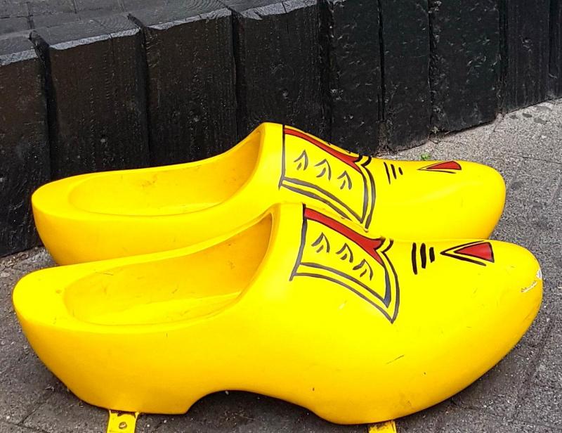 Wielkie chodaki 2 Żółte drewniaki z czerwono-czarnym wzorem, stojące na chodniku przy murze.