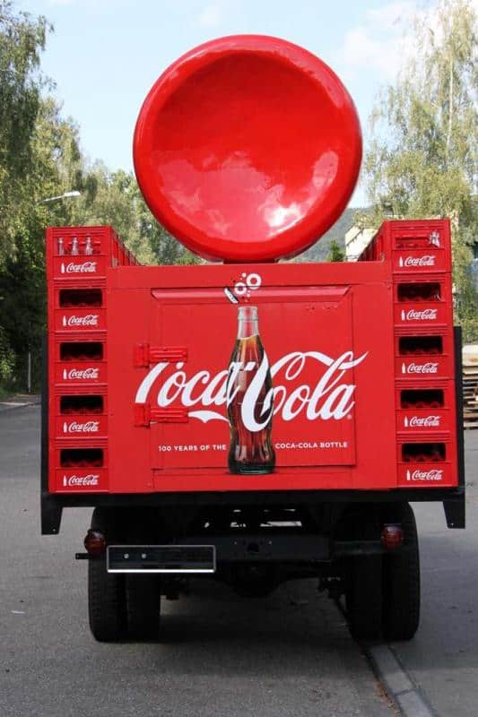 Tył czerwonej ciężarówki promującej Coca-Colę z dużą butelką i logo marki.
