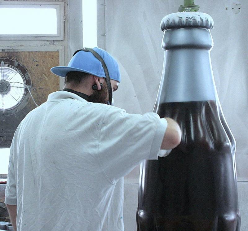 Mężczyzna w niebieskiej czapce lakieruje dużą butelkę.