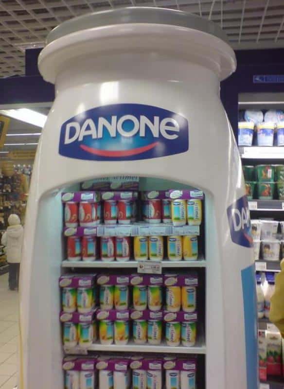 Reklamowe urządzenie chłodnicze Actimel 1 Lodówka w kształcie butelki z logo Danone, wypełniona produktami jogurtowymi w sklepie.