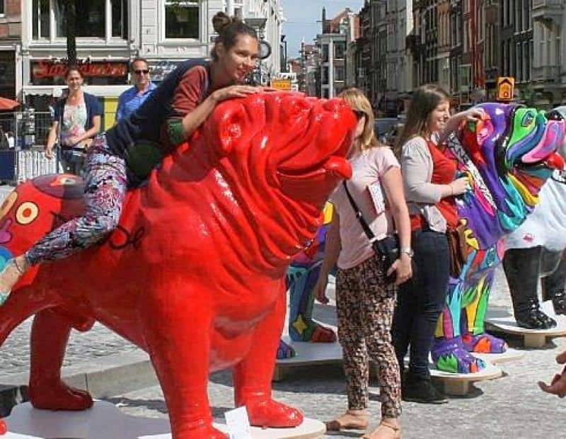 Ludzie wchodzący w interakcję z kolorowymi rzeźbami buldogów na ulicy w mieście.