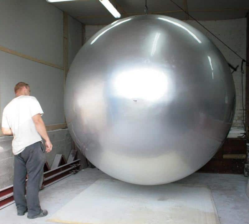 Wielka kula w przestrzeni miejskiej 4 Mężczyzna stojący obok ogromnej, srebrnej kuli w hangarze.