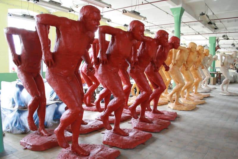 Promocja mistrzostw świata IAAF 2 Figury męskich postaci w dziwnie wykręconej pozie, pomalowane na czerwono, pomarańczowo i biało, ustawione w rzędzie w przestrzeni magazynowej.