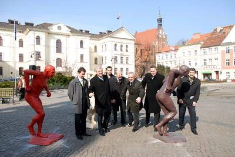 Promocja mistrzostw świata IAAF 3 Grupa mężczyzn na placu z rzeźbami w mieście z budynkami w tle.