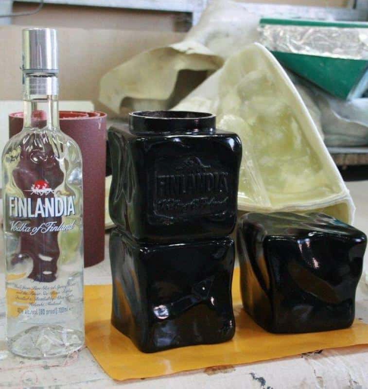 Opakowanie promocyjne Finlandia 2 Butelka Finlandia Vodka To/1750 ml oraz trzy czarne, zdeformowane butelki Finlandia umieszczone na stole roboczym.