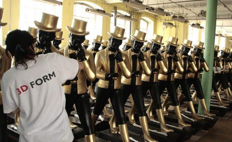 Duże figury Johnnie Walker 4 Rzędy manekinów ubrane we złote garnitury i cylindry, osoba w białej koszulce z napisem