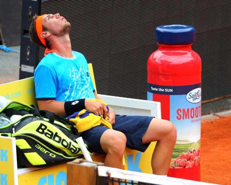 oryg_064490685_1129949550544944_1465385417682452480_o Mężczyzna w sportowym stroju siedzi na ławce obok dużej torby tenisowej i dużej butelki napoju, odchylając głowę do tyłu.