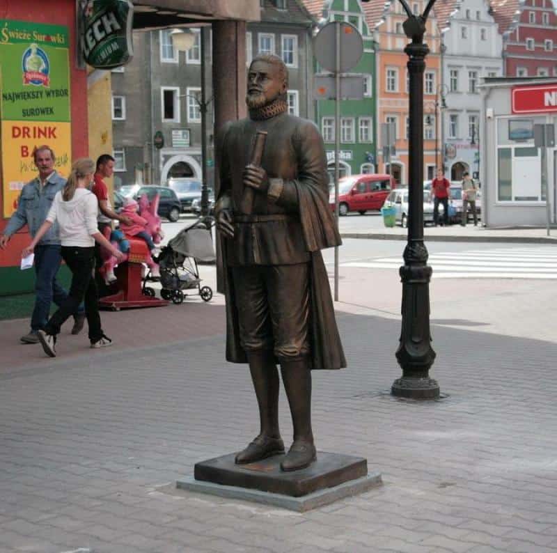 Pomnik mężczyzny w historycznym stroju trzymającego zwój na ulicy w mieście.