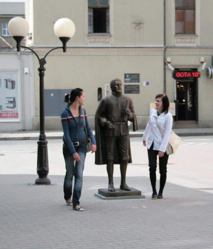 Dwie kobiety obok rzeźby mężczyzny na chodniku w mieście.