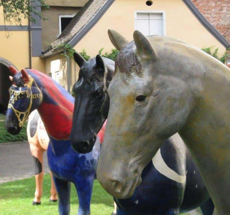 Eventowe figury koni 4 Trzy kolorowe rzeźby koni ustawione w ogrodzie przed domem.