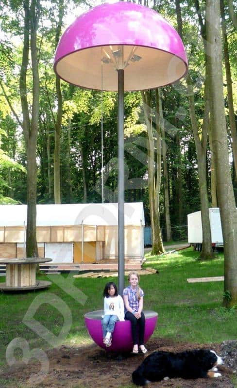 Lampy festiwalowe 2 Dwoje dzieci siedzących na różowej huśtawce w kształcie grzyba w lesie, obok leży czarny pies.