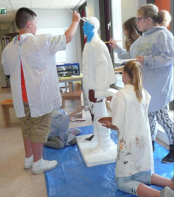 Rzeźby górników 2 Dzieci malują stojącą rzeźbę człowieka w szkolnej sali.