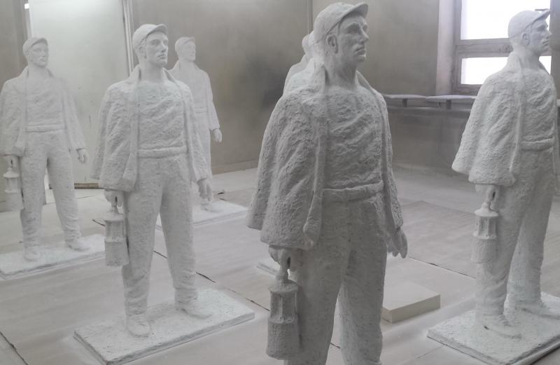 Rzeźby górników 4 Posągi górników trzymających lampy górnicze ustawione w pomieszczeniu.