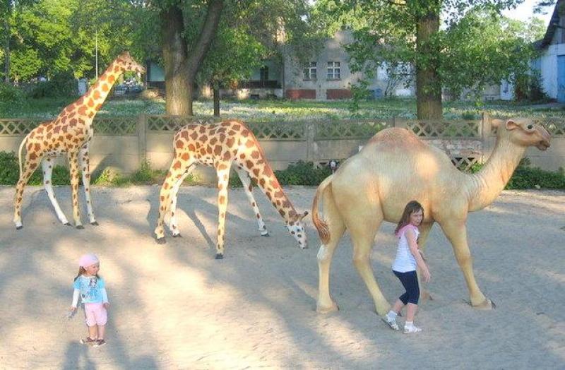 Figury w parku tematycznym 4 Dzieci bawiące się obok figur żyraf i wielbłąda w parku.