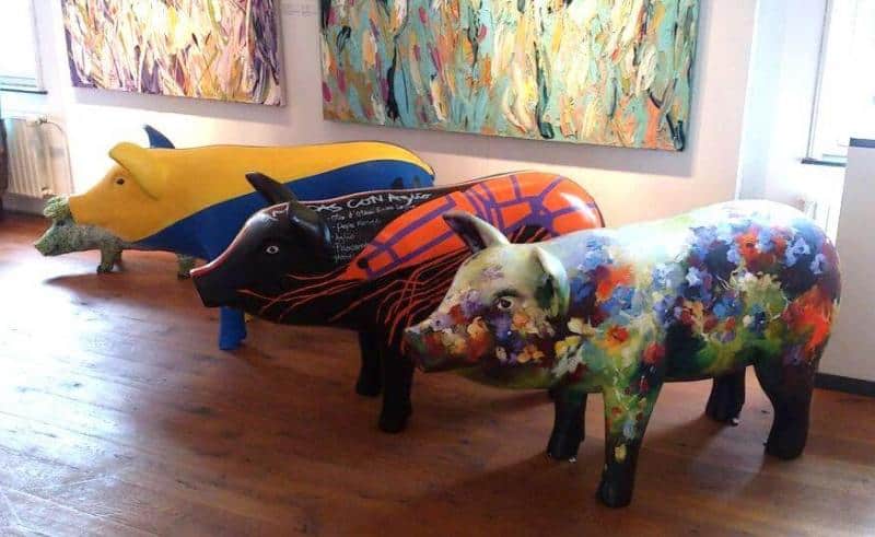 Artystycznie malowane figury zwierząt 1 Trzy kolorowe rzeźby świni w galerii sztuki, każda ozdobiona różnorodnymi wzorami i malowidłami.