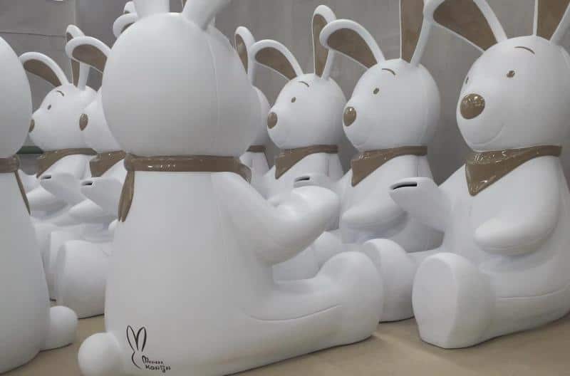 Królik skarbonka 3 Białe figurki królików z brązowymi detalami siedzące w rzędach.