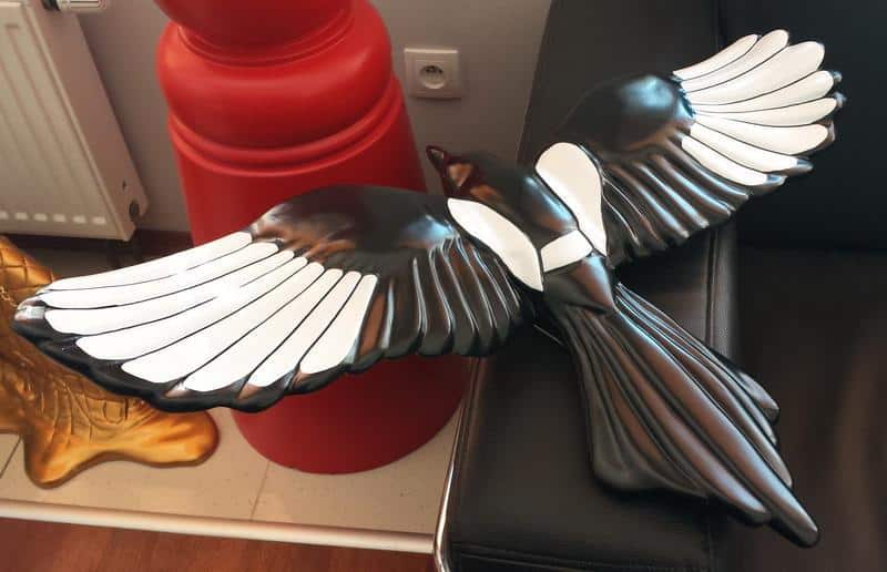 Rój Srok w Berlinie 3 Czarna rzeźba ptaka z rozłożonymi skrzydłami leżąca na kanapie.