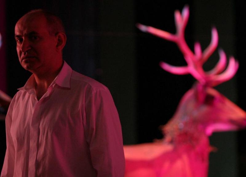 Elementy scenografii dla Teatru Dramatycznego Miasta Stołecznego Warszawy 2 Mężczyzna w białej koszuli stojący obok różowo podświetlonego jelenia.