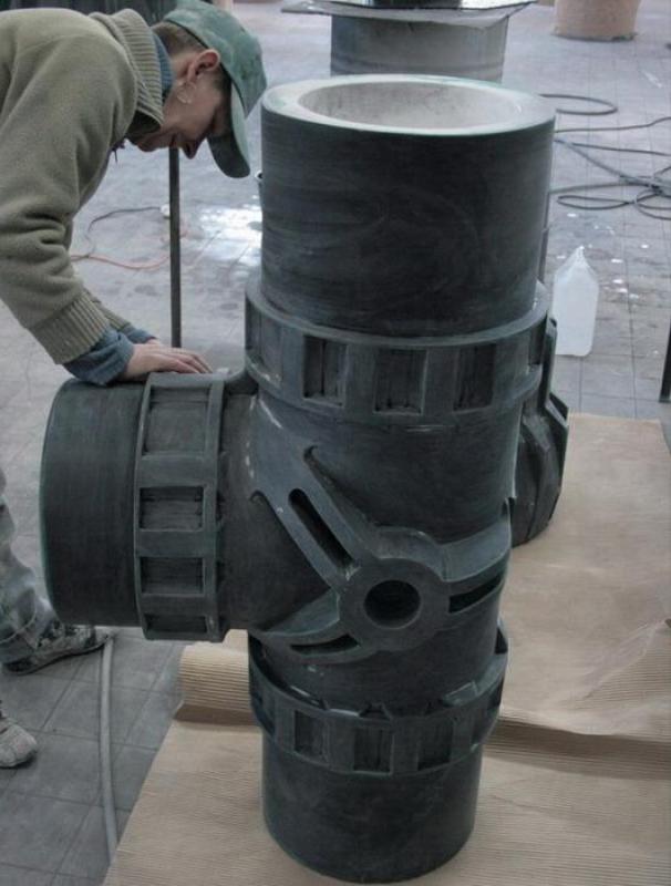 Trójnik - kształtka rurowa 3 Mężczyzna w warsztacie pochylający się nad dużym rzeźbionym modelem krzyżowego połączenia rur.