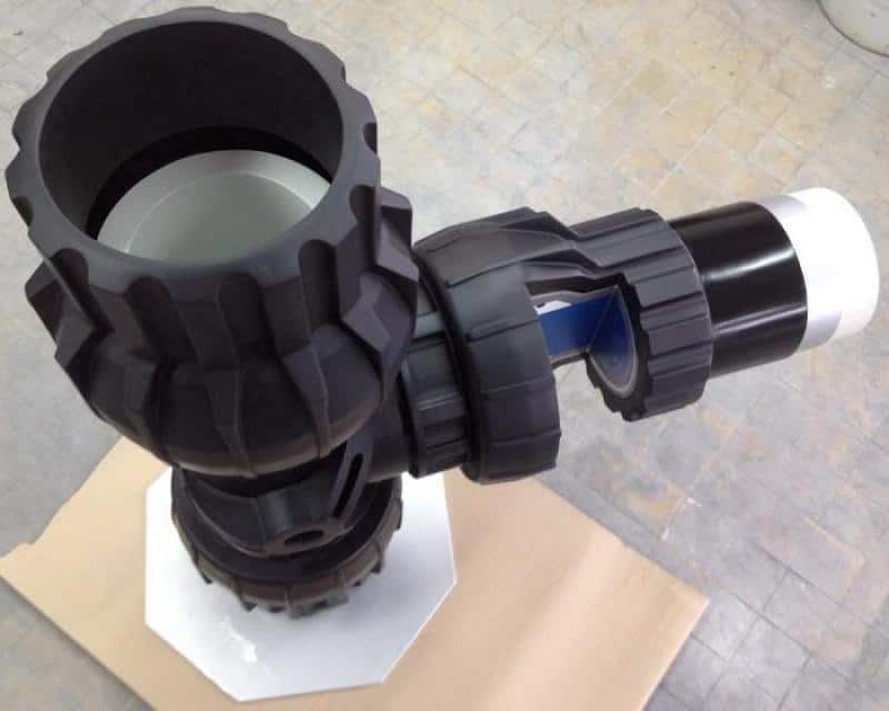 Trójnik - kształtka rurowa 4 Czarny element mechaniczny o skomplikowanej budowie, z przegubem i uchwytem, na tle kartonowej powierzchni.