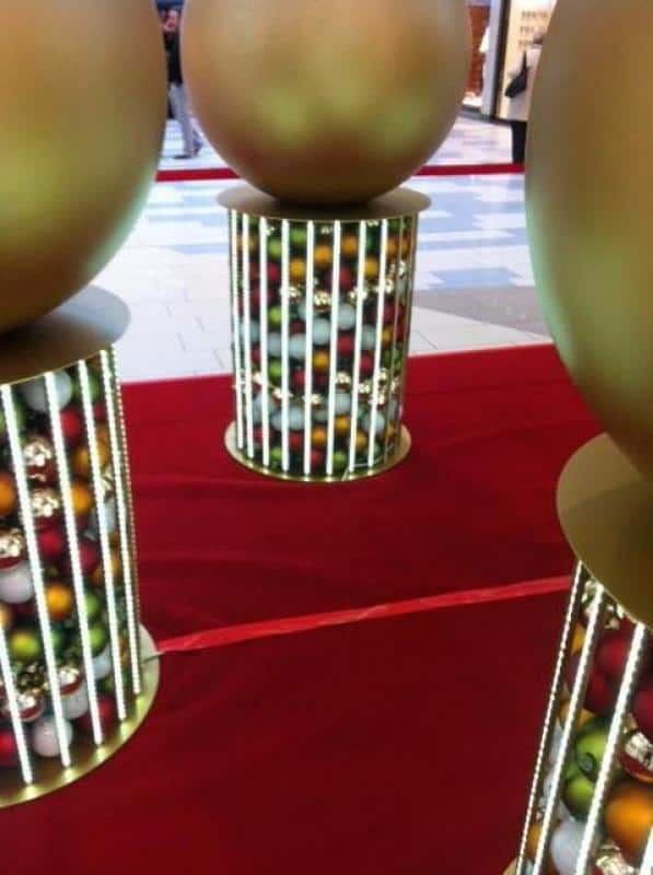 Podświetlane bombki świąteczne 3 Duże złote kule na cylindrycznych stojakach w galerii handlowej.