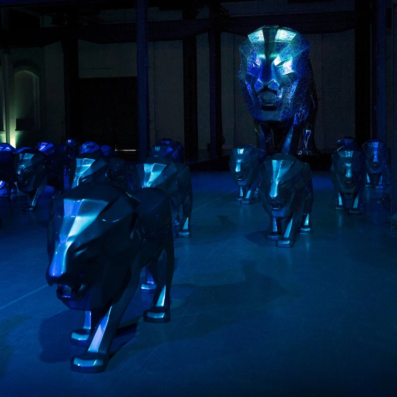 Metalowe rzeźby lwów w ciemnym, niebiesko oświetlonym pomieszczeniu.