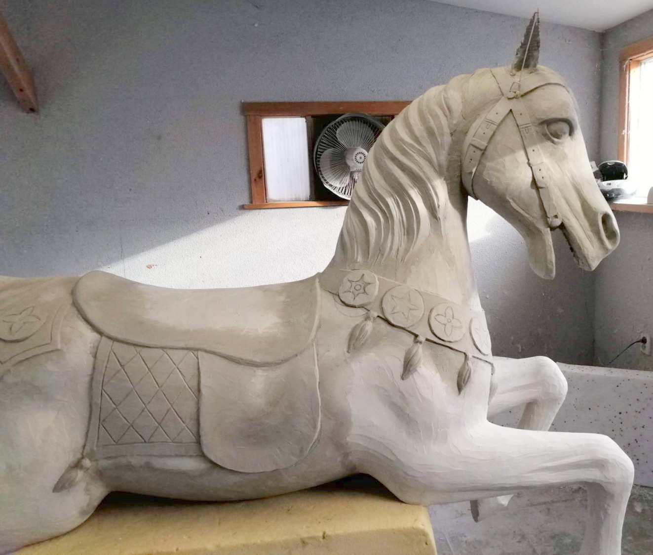 Karuzela wyjątkowych jednorożców 5 Koń rzeźbiony w drewnie z siodłem i ozdobami w pracowni.