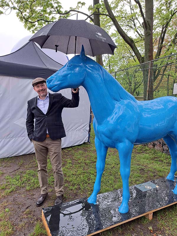 Mężczyzna trzymający parasol nad niebieską statuetką konia.
