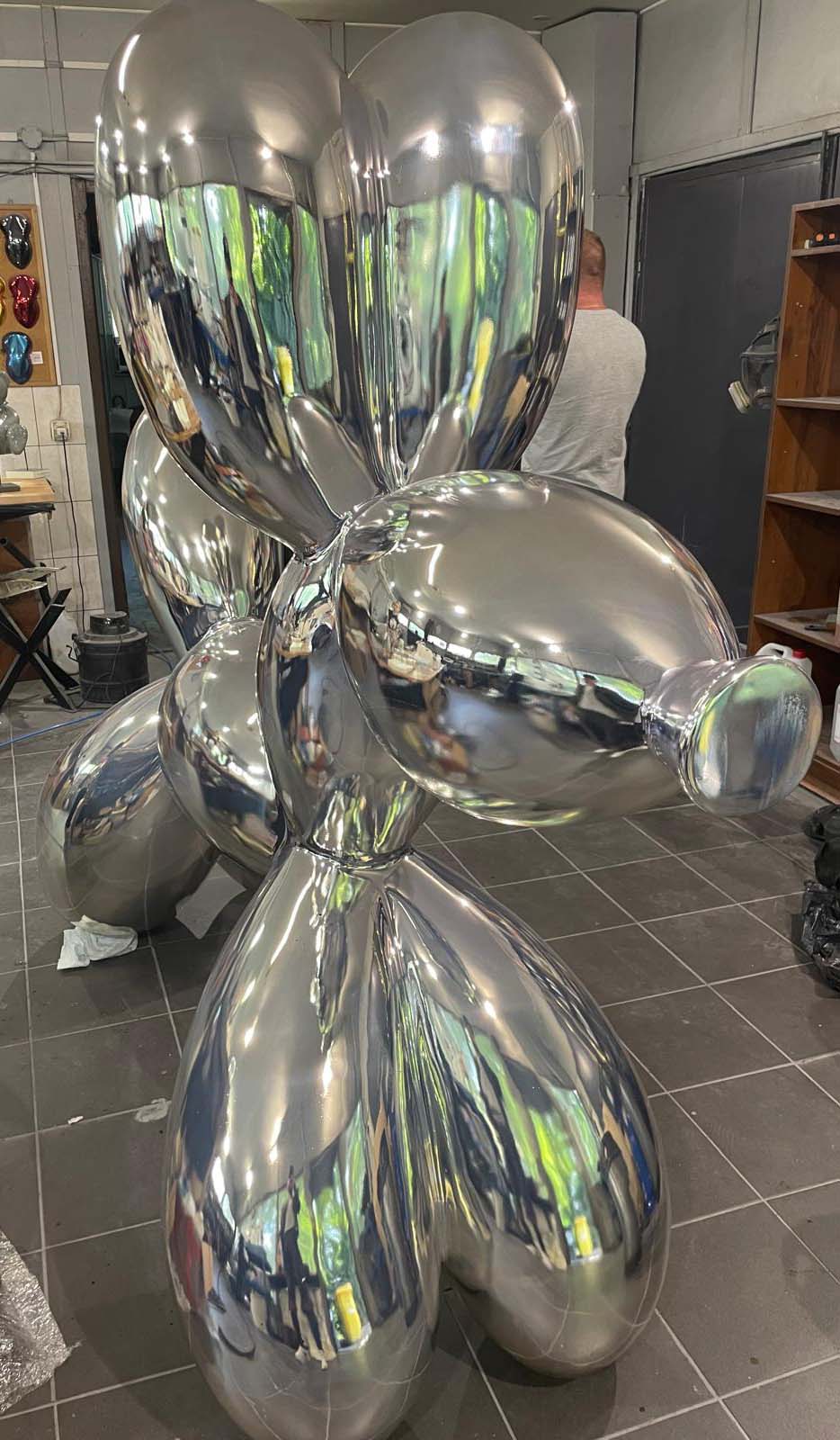 Srebrna rzeźba przypominająca balonowego psa w pracowni artystycznej.