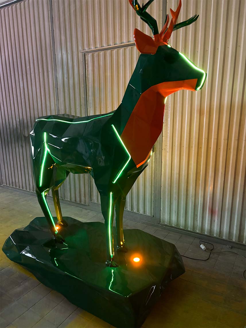 Rzeźba jelenia z neonowymi światłami na stalowym podłożu w hali przemysłowej.