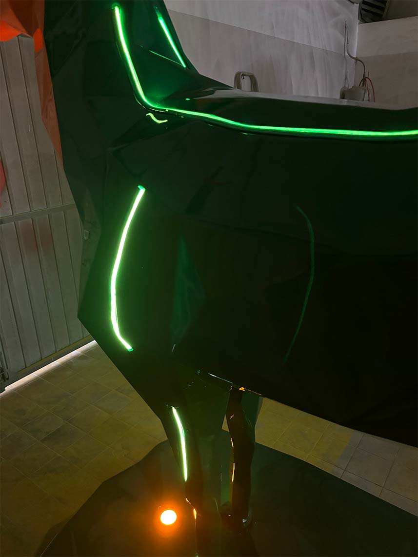 Zdjęcie przedstawia ciemny obiekt o błyszczącej powierzchni z podświetleniami w kolorze zielonym, znajdujący się w zamkniętym pomieszczeniu.