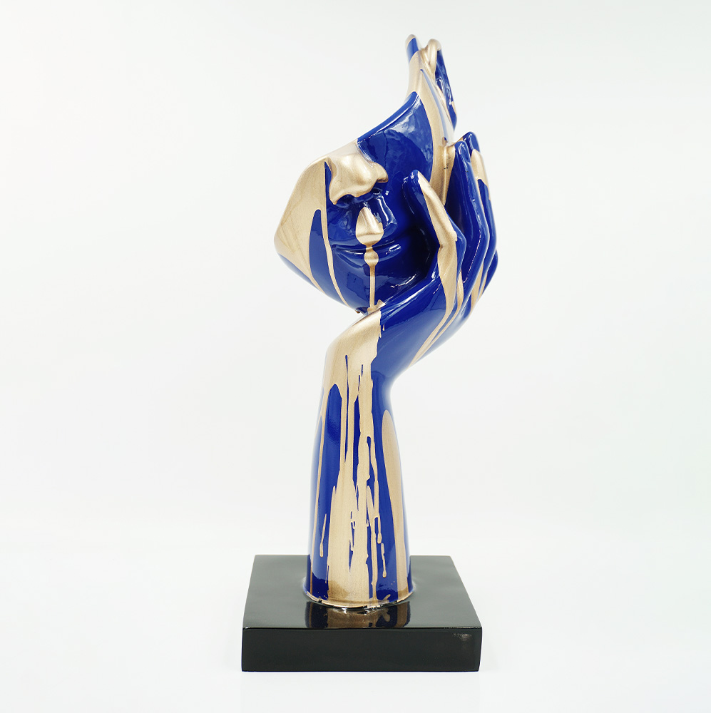 Mała Maska Na Podstawie - Motyw IV 1 Rzeźba przedstawiająca dłoń z twarzą w odcieniach niebieskiego i złotego, stojąca na czarnej podstawie na białym tle