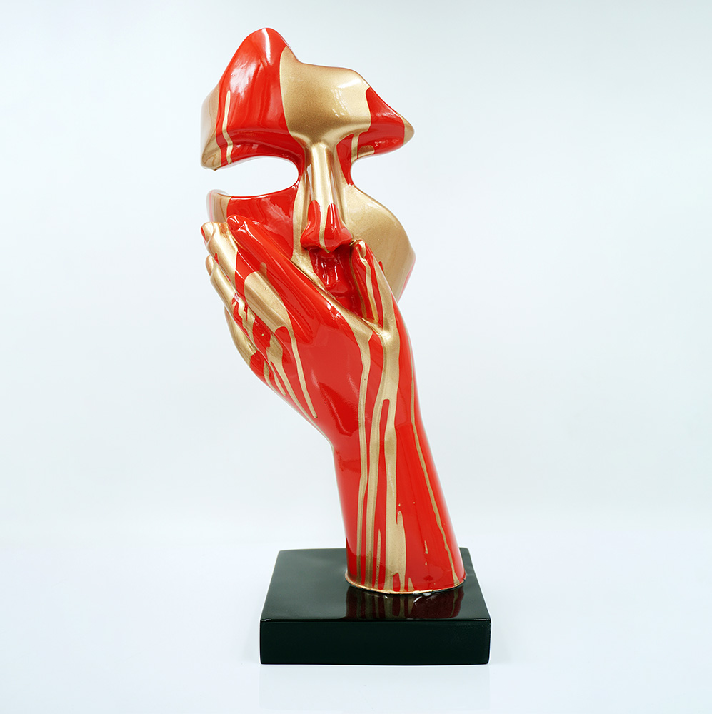 Mała Maska Na Podstawie - Motyw III 2 Rzeźba przedstawiająca czerwoną i złotą abstrakcyjną formę dłoni podtrzymującej fragment twarzy, stojąca na czarnej podstawie na białym tle.