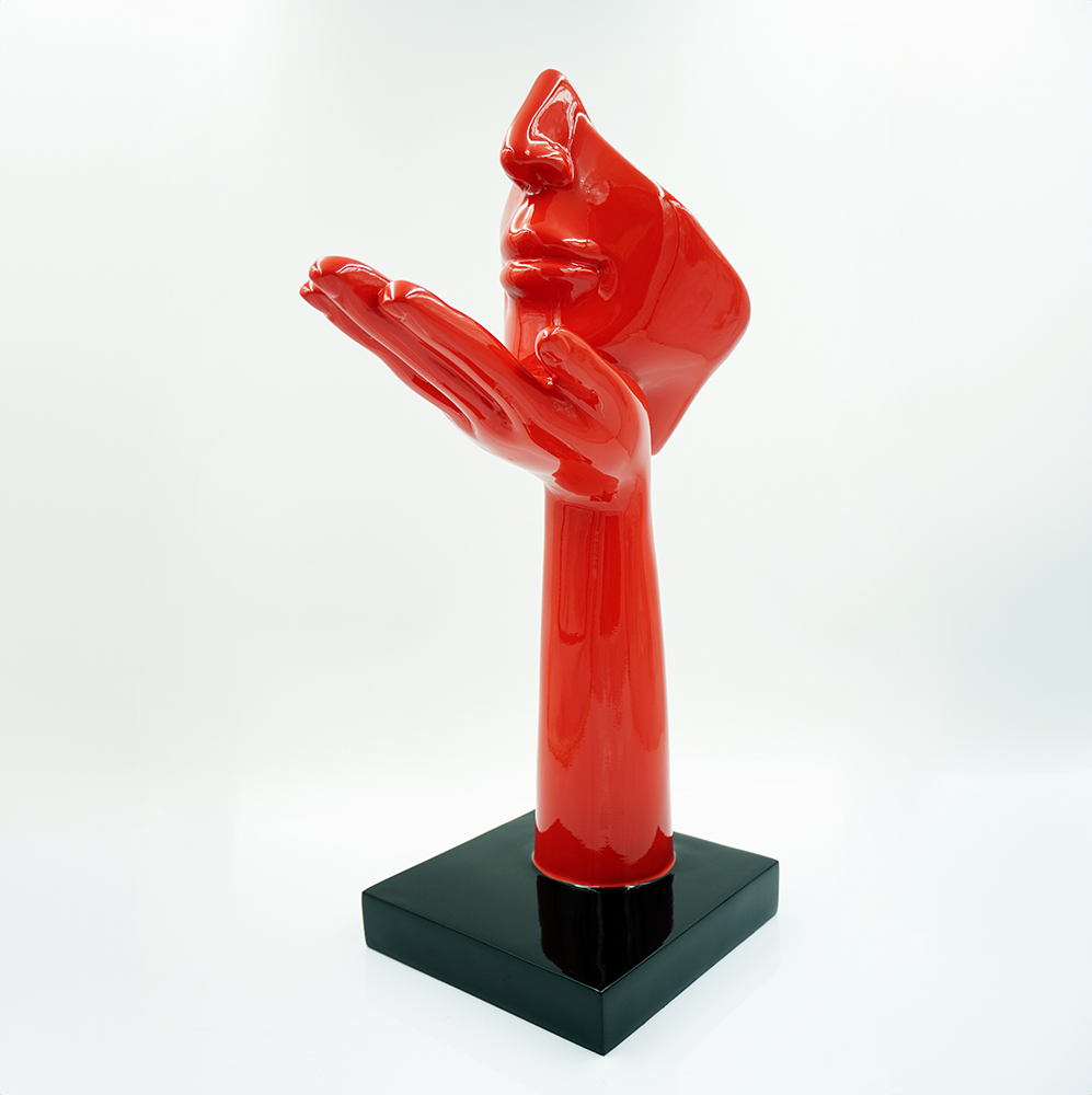 Mała Maska Na Podstawie - Motyw I 3 Czerwona abstrakcyjna rzeźba przedstawiająca wychyloną twarz i dłoń, stojąca na czarnej kwadratowej podstawie na jasnym tle.