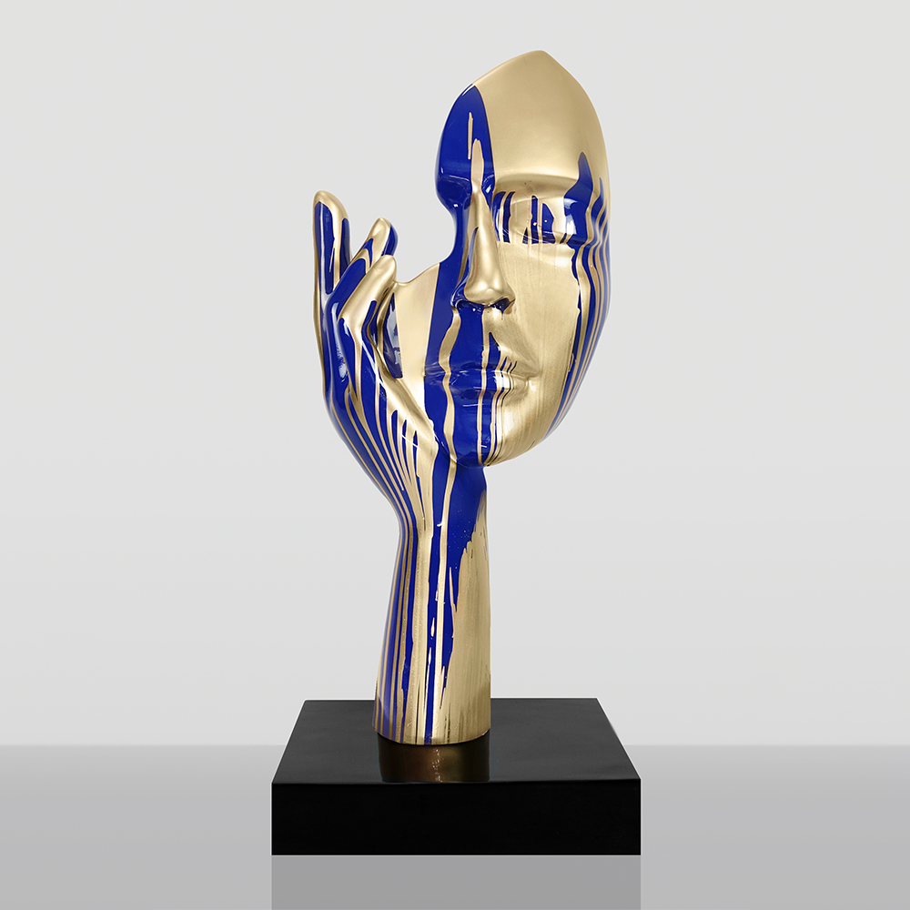 Średniej Wielkości 120CM Maska Niebieska Na Podstawie - Złoty Trash 1 Złoto-granatowa abstrakcyjna rzeźba przedstawiająca twarz i dłoń z pionowymi akcentami na czarnej podstawie na szarym tle