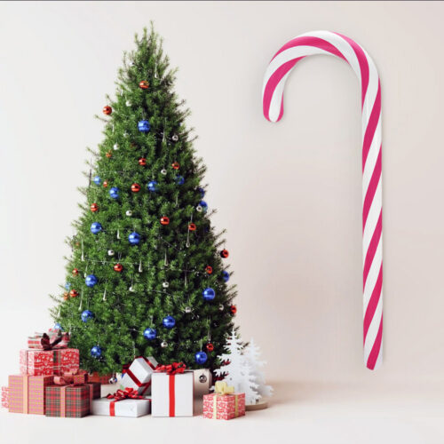 Choinka udekorowana czerwonymi, niebieskimi i srebrnymi bombkami, otoczona prezentami w czerwonych i białych papierach, obok duża lizakowa laska w biało-różowe paski na jasnym tle.
