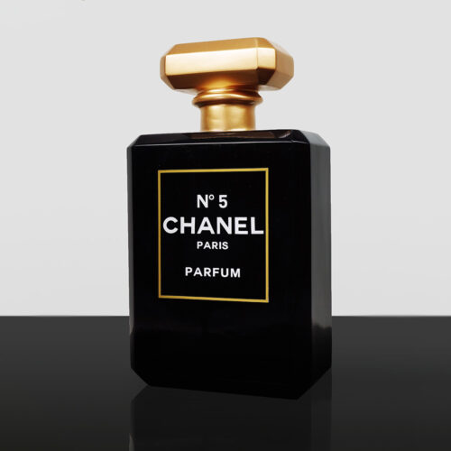 czarna butelka perfum Chanel No 5 z złotym korkiem na czarnej powierzchni na szarym tle